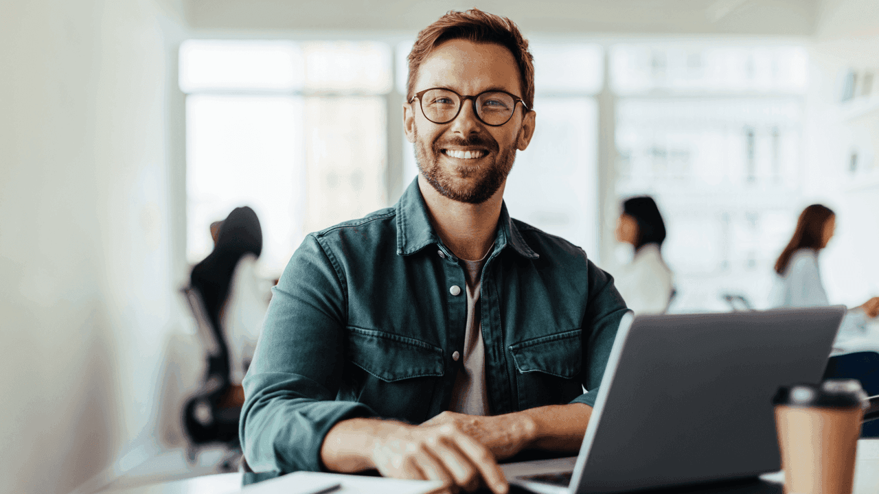 Mies katsoo toimistolla hymyillen kameraan