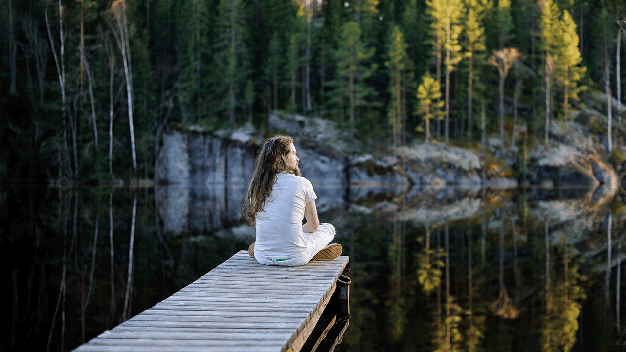 Man sits on deck at a calm lake.
