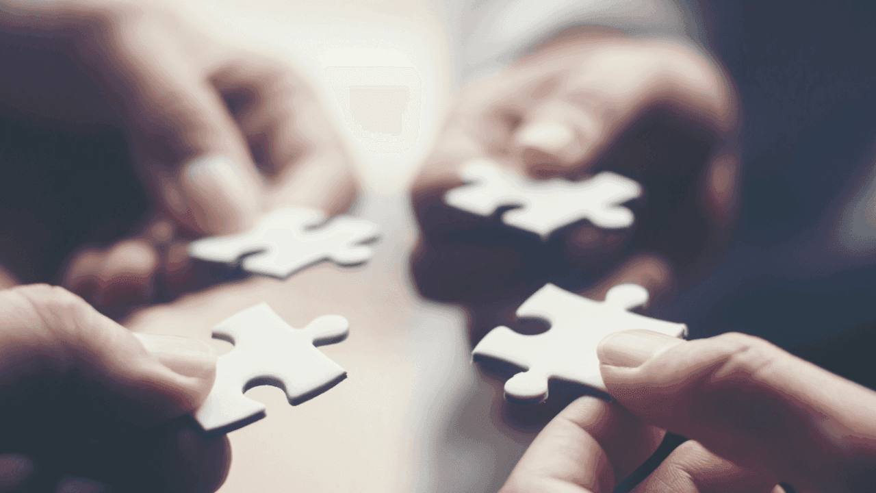 Neljä kättä yhdistävät palapelin paloja kuvaten yhteistyötä