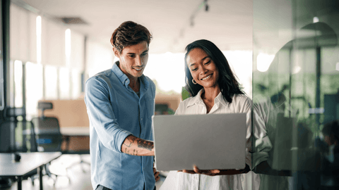 Nuori opastaa toista koneen ääressä toimistolla